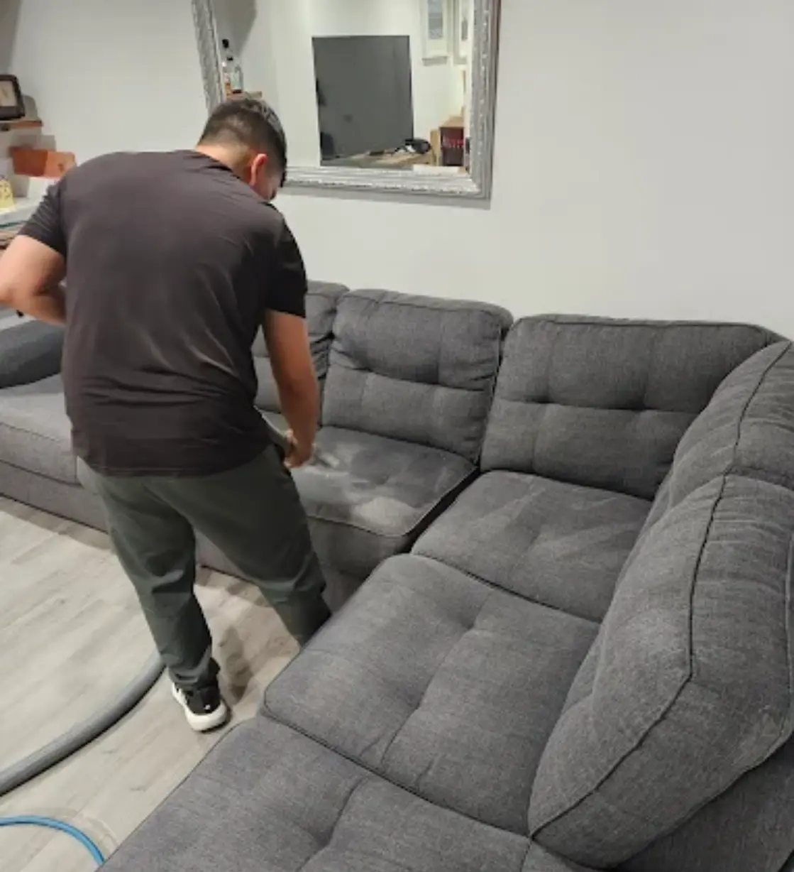 Green Carpet Cleaning Long Island technician cleaning a large gray fabric sectional sofa in a living room
