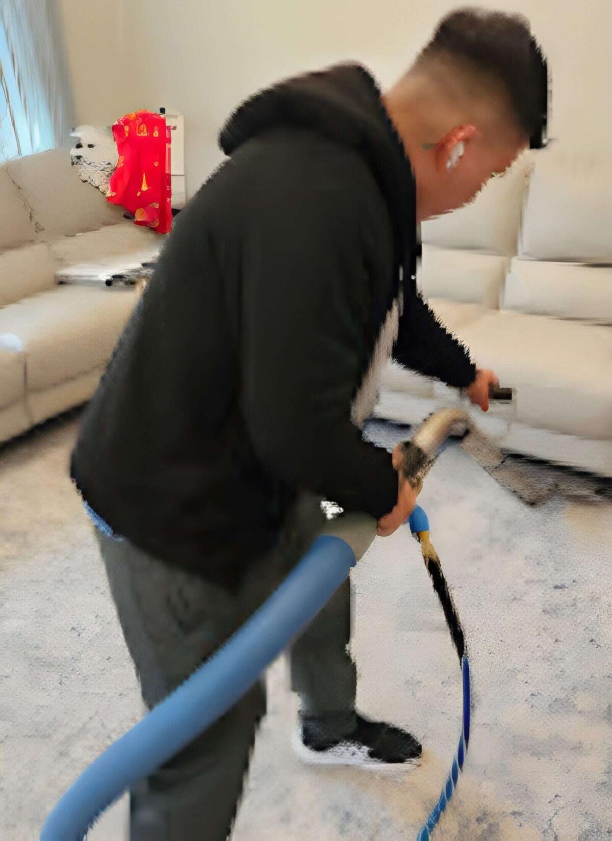 Technician cleaning a light gray area rug in front of cream colored sofas with a wand and blue hose